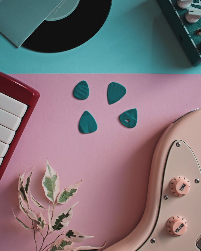 Flat lay of guitar, vinyl record, and keyboard on pastel background.